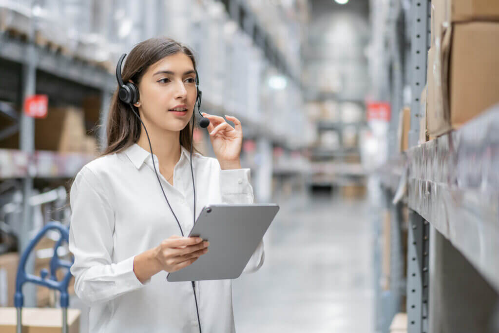 Portrait of Aztec Fleet Logistics warehouse woman staff using digital tablet and talking to customer with headset working in Aztec Fleet warehouse.